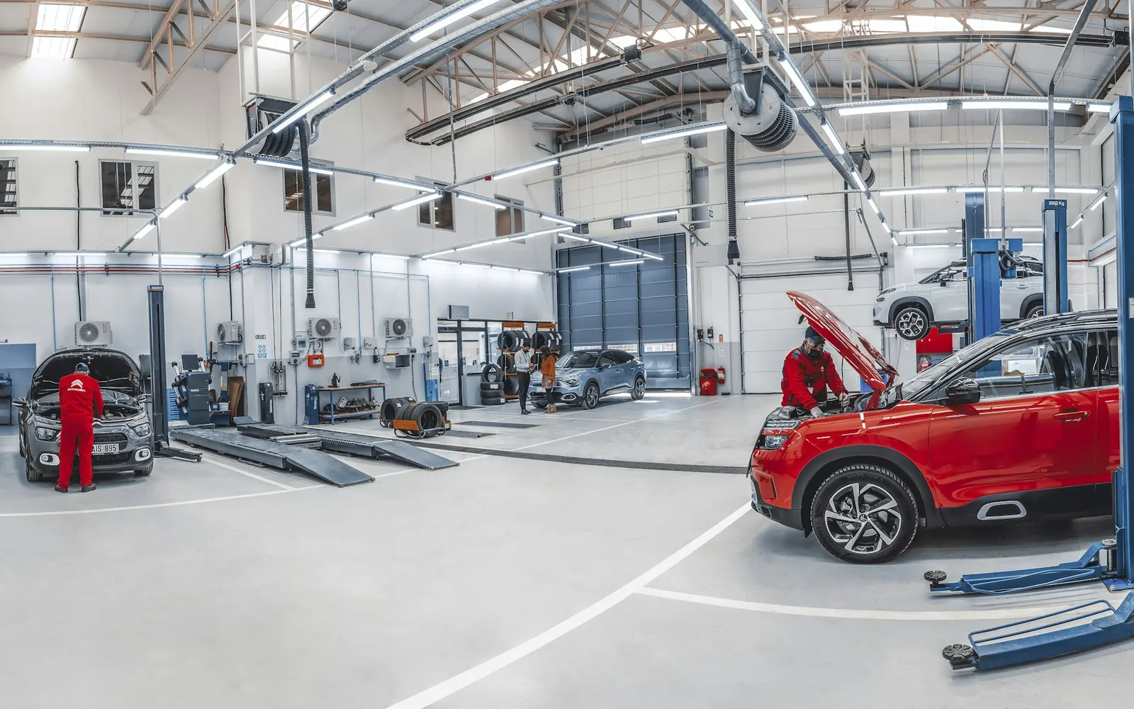A bright repair workshop with cars on lifts and a technician working under an open bonnet.
